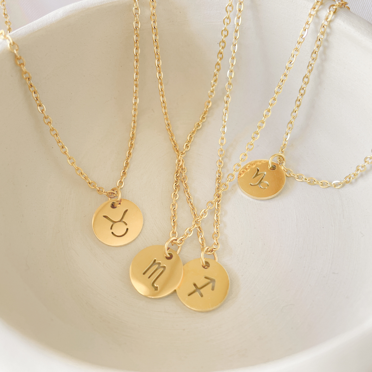 Gold monogramed circular pendants laying in a white bowl