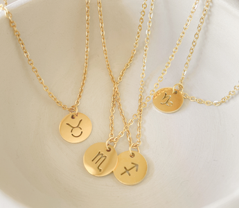 Gold monogramed circular pendants laying in a white bowl