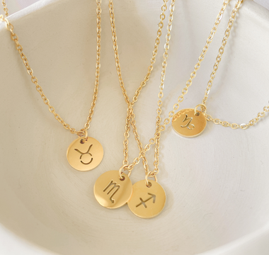 Gold monogramed circular pendants laying in a white bowl